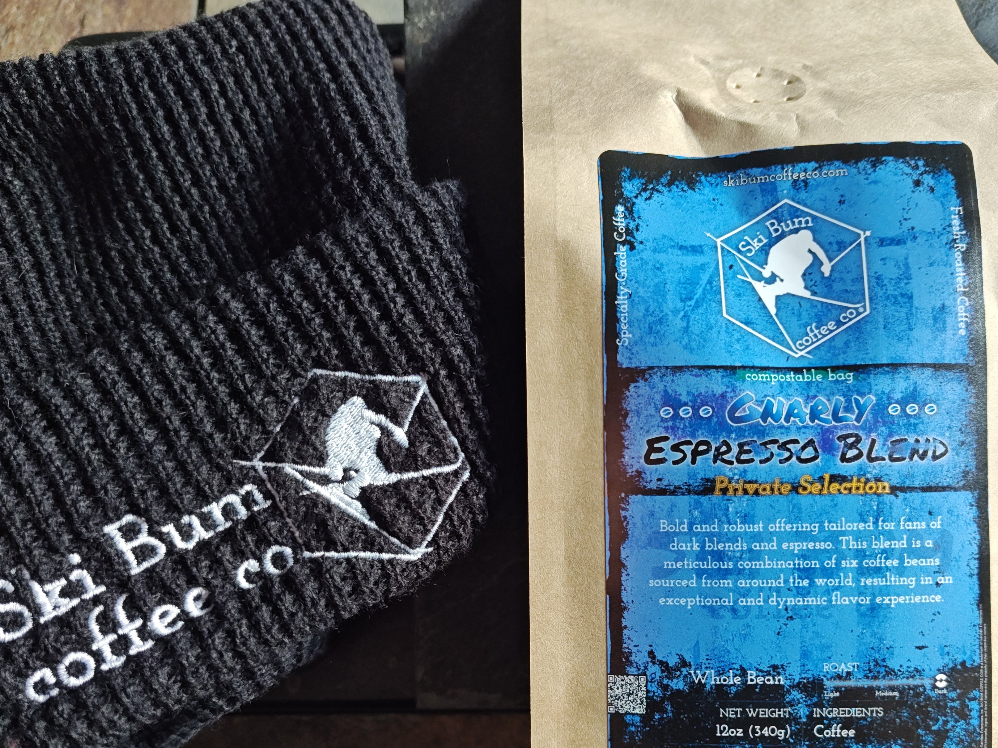 Black knit beanie with 'Ski Bum Coffee Co.' logo and a compostable coffee bag of 'Gnarly Espresso Blend', on a stone surface.